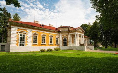 Samchyky Palace displaying historical architecture and grandeur, featuring yellow walls, a red roof, white columns, and green manicured lawns under a summer sky in Khmelnytskyi region