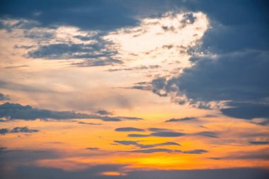 Gökyüzü parlak turuncu ve sarı renklerle boyanır yumuşak mavi gri bulutlara dönüşür dramatik ama sakin bir günbatımı bulutu ufuk boyunca sıcak ve serin tonlarda yaratır.