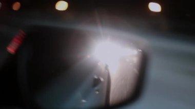 Arkadaki aracın parlak farları gece sürüşü sırasında dikiz aynasından görüldü, aşırı parıltı, soyut ışık şekilleri, trafik tehlikesi, kentsel manzara karışıklığı