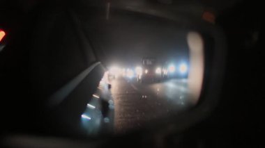 Aracın arkasından gelen kör farlar gece sürüşü sırasında dikiz aynasından görülüyor, araba kapısı ve trafik ışığının yakın görüntüsü.