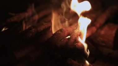 Koyu sarı ve turuncu alevlerle yanan kuru odunların yakın görüntüsü düşük ışıkta ısı, doku ve parlayan közleri gösteriyor.