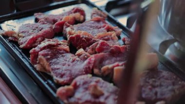 Baharatlı çiğ biftekler, açık hava pişirme sürecine yakın sıcaklıkta, cızırdayan yağ ve dumanlı buhar ile sıcak düz yüzeyde ızgara yapıyor.