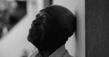 Afro-Amerikalı yaşlı adam dikkatlice yukarı bakıyor, siyah beyaz bir duvara yaslanıyor, bilgelik, umut ve içgözlem ifade ediyor.