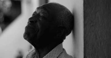 Afro-Amerikalı yaşlı adam dikkatlice yukarı bakıyor, siyah beyaz bir duvara yaslanıyor, bilgelik, umut ve içgözlem ifade ediyor.