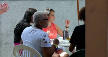 Çeşitli bireylerden oluşan bir grup açık hava masasında toplandı, sohbet ve etkileşimle meşguller, çok kültürlü dinamik, günlük yaşam anı