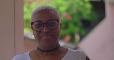 Gözlüklü gülümseyen kadın doğrudan kameraya bakıyor, doğal ortamında, neşeli ve kendine güvenen ifade, bireyselliği kucaklayan ve enerjik kişiliğe sahip.