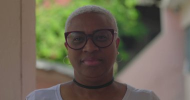 Latin kökenli, kısa beyaz saçlı, gözlüklü, sakin ve kendinden emin, canlı ve doğal bir şekilde dışarı bakan Latin bir kadın.