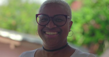 Gülümseyen kıvırcık saçlı, siyah gömlekli, kendine güveni ve neşe saçan, yeşil, sıcak ve dost canlısı, güler yüzlü genç İspanyol çocuk.