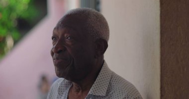 Sakin bir ifadeyle Afrika kökenli yaşlı bir adam, düşünceli bir şekilde yan tarafa bakıyor, açık havada yumuşak doğal ışık ve canlı yeşillikle, bilgelik ve dinginlik yayıyor.