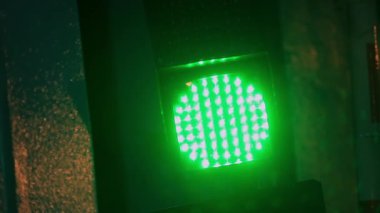 Kentsel sokak ortamında gece parlayan yeşil LED trafik ışığı yüzeyinde yağmur damlacıkları, canlı fütüristik atmosfer yaratıyor ve kentsel modern altyapıyı yansıtıyor