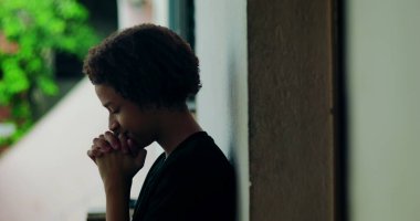 Afrika kökenli, kıvırcık saçlı, gözleri kapalı, açık havada dua eden elleri birbirine kenetlenmiş, derin ruhsal yansıması olan, huzurlu bir çocuk.