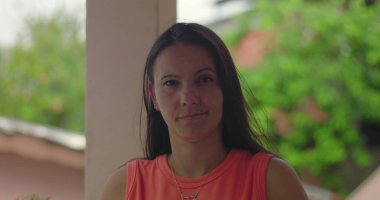 Normal giyinmiş ciddi bir kadın, doğal arka planı olan sakin ve aklı başında bir şekilde dışarıda duruyor.