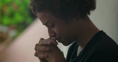 Duygusal sıkıntı içindeki genç bir çocuk, elleri yüzünü kapatıyor, ağlıyor, duvara yaslanıyor, Afrika kökenli, açık hava manzaralı, yakın plan.