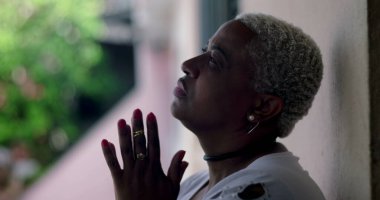 Bir Latin Latin kökenli Afrikalı kadın kısa kıvırcık saçlı derin duada ya da elleri birbirine kenetlenmiş yansımalı duygusal an, maneviyat, inanca odaklan.