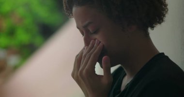 Duygusal sıkıntı içindeki genç bir çocuk, elleri yüzünü kapatıyor, ağlıyor, duvara yaslanıyor, Afrika kökenli, açık hava manzaralı, yakın plan.