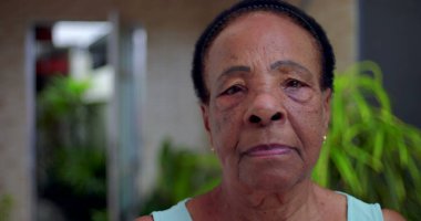 Ciddi ve sakin bir ifadeye sahip yaşlı Afrikalı Amerikalı kadının yakın plan portresi, açık hava bahçesi geçmişi, bilgelik anlayışı, güç ve son sınıf öğrencilerinin varlığı.