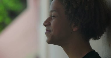 Genç bir İspanyol çocuk gülümsüyor, duvara karşı duruyor, neşeli bir ifade, Afrika kökenli, olumlu duygusal rahatlama, açık hava düzeni, yakın çekim