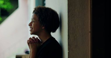 Afrika kökenli, kıvırcık saçlı, gözleri kapalı, açık havada dua eden elleri birbirine kenetlenmiş, derin ruhsal yansıması olan, huzurlu bir çocuk.