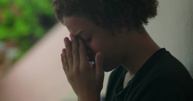 Duygusal sıkıntı içindeki genç bir çocuk, elleri yüzünü kapatıyor, ağlıyor, duvara yaslanıyor, Afrika kökenli, açık hava manzaralı, yakın plan.