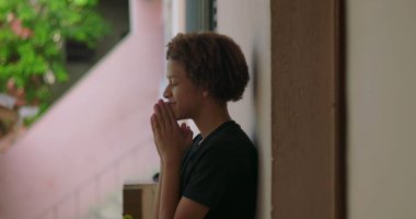 Afrika kökenli, kıvırcık saçlı, gözleri kapalı, elleri dua ederken sımsıkı bağlanmış, ruhsal, sessiz bir açık hava anını yansıtan, derin düşüncelere dalmış, içsel bir duraksama yaşayan Latin kökenli genç bir çocuk.