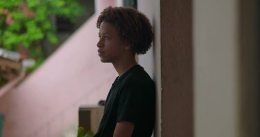 Afrika kökenli, kıvırcık saçlı, derin düşüncelere dalmış, açık havada yansıyan, barışçıl bir ifade, yukarıya bakan, içe dönük bir çocuk.