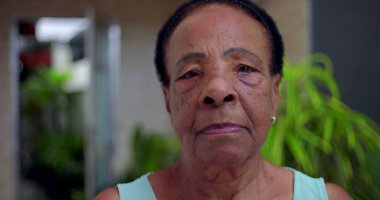 Ciddi ve sakin bir ifadeye sahip yaşlı Afrikalı Amerikalı kadının yakın plan portresi, açık hava bahçesi geçmişi, bilgelik anlayışı, güç ve son sınıf öğrencilerinin varlığı.