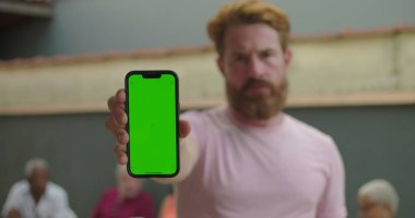 Elinde yeşil ekranlı akıllı telefon tutan adam, ciddi ifade, dışarıda duran, arka planda bulanık insanlar, kişiselleştirilebilir ekran odağı.