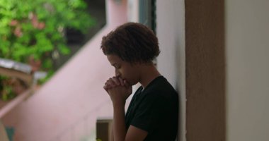 Afrika kökenli, kıvırcık saçlı, gözleri kapalı, elleri dua ederken sımsıkı bağlanmış, ruhsal, sessiz bir açık hava anını yansıtan, derin düşüncelere dalmış, içsel bir duraksama yaşayan Latin kökenli genç bir çocuk.