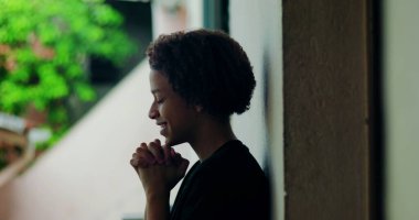 Afrika kökenli, kıvırcık saçlı, gözleri kapalı, açık havada dua eden elleri birbirine kenetlenmiş, derin ruhsal yansıması olan, huzurlu bir çocuk.