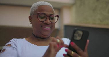 Afrika kökenli bir kadının akıllı telefon kullanarak, odaklanmış ve meşgul bir şekilde dış mekanda canlı çiviler ve aksesuarlar gösteren bir fotoğrafı.