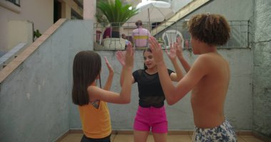 Avluda neşeli kardeşler alkışlıyor, gülümsüyor ve neşeli oyunlar oynuyorlar. Kaygısız çocukluk eğlencesi, enerjik kahkahalar ve yakın aile bağları.