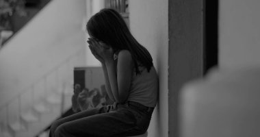 Elleri kapalı, gözleri kapalı, duygusal bir anda yerde oturan genç bir çocuk, sakin, yansıtıcı şehir ortamında travma ve üzüntü ile başa çıkıyor, siyah ve beyaz