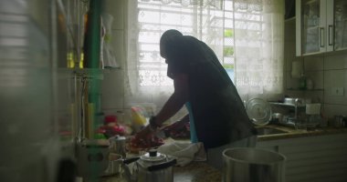 Afrika kökenli bir adam mutfak tezgahında yemek kesiyor, yemek hazırlıyor, günlük anlarını sergiliyor, aile hayatı ve yemek pişirme sanatı.