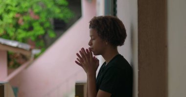 Afrika kökenli, kıvırcık saçlı, gözleri kapalı, elleri dua ederken sımsıkı bağlanmış, ruhsal, sessiz bir açık hava anını yansıtan, derin düşüncelere dalmış, içsel bir duraksama yaşayan Latin kökenli genç bir çocuk.