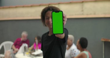 Afrika kökenli, yeşil ekranlı, krom anahtarlı, arka planda gelişigüzel sohbetlerin keyfini çıkaran çeşitli yetişkinlerin bulunduğu bir sosyal ortamda sergilenen akıllı telefon.