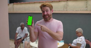 Krom tuşlu yeşil ekranlı akıllı telefonu tutan adam, kendinden emin bir şekilde gülümseyen, dijital içeriği gösteren, açık hava ayarları, teknoloji odaklı, gelişigüzel an, bağlantı ekranı