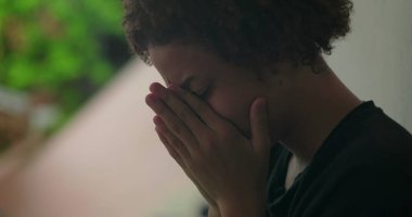 Duygusal sıkıntı içindeki genç bir çocuk, elleri yüzünü kapatıyor, ağlıyor, duvara yaslanıyor, Afrika kökenli, açık hava manzaralı, yakın plan.