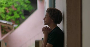 Afrika kökenli, kıvırcık saçlı, gözleri kapalı, elleri dua ederken sımsıkı bağlanmış, ruhsal, sessiz bir açık hava anını yansıtan, derin düşüncelere dalmış, içsel bir duraksama yaşayan Latin kökenli genç bir çocuk.