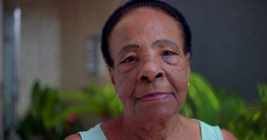 Ciddi ve sakin bir ifadeye sahip yaşlı Afrikalı Amerikalı kadının yakın plan portresi, açık hava bahçesi geçmişi, bilgelik anlayışı, güç ve son sınıf öğrencilerinin varlığı.