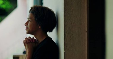 Afrika kökenli, kıvırcık saçlı, gözleri kapalı, açık havada dua eden elleri birbirine kenetlenmiş, derin ruhsal yansıması olan, huzurlu bir çocuk.