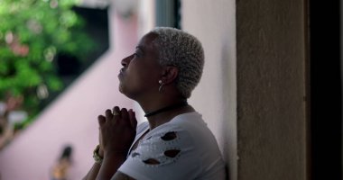 Derin düşüncelere sahip bir kadın, duvara yaslanmış, elleri birbirine kenetlenmiş dua, duygusal rahatlama, Afrika kökenli, yansıtıcı an, açık hava