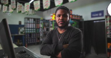 Bir boyacıda kolları çapraz duran kendine güvenen genç adam profesyonelliği, liderliği ve perakende sektöründe güçlü bir iş ahlakını temsil ediyor.