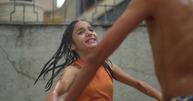 Gençler yağmurda neşeli bir an yaşıyor, el ele tutuşup gülümsüyor, arkadaşlığı, birliği ve gençliği coşkulu bir ortamda kutluyorlar.