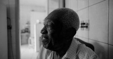 Afrika kökenli yaşlı bir adam fayanslı bir mutfakta neşeyle gülüyor, siyah beyaz bir portre, bir ev ortamında mutluluk, bağlantı ve bilgeliği vurguluyor.