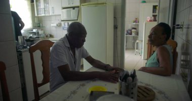 Yaşlı bir çift Afrika kökenli yemek masasında sohbet ediyorlar, aile içi etkileşim bir yuva ortamında yakınlık, sıcaklık ve günlük yaşamı yakalıyorlar.