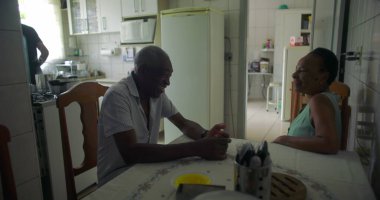 Yaşlı bir çift Afrika kökenli yemek masasında sohbet ediyorlar, aile içi etkileşim bir yuva ortamında yakınlık, sıcaklık ve günlük yaşamı yakalıyorlar.