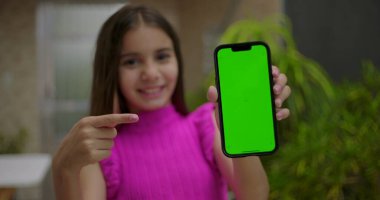 Elinde yeşil ekran krom anahtarı olan akıllı telefonu tutan, neşeli bir ifadeyle boş ekrana bakan, açık bir evde kişiselleştirilebilir içeriği gösteren genç bir kız.