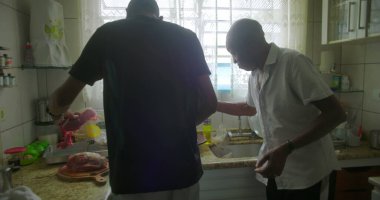 Afrika kökenli yaşlı bir adam elinde neşeli bir ifadeyle bir et parçası tutuyor, kültürel gelenekleri ve aşçılık hazırlıklarını vurguluyor.