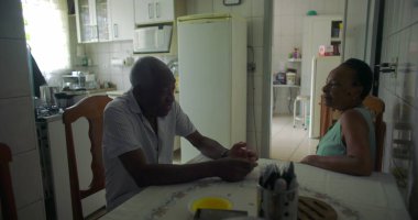 Yaşlı bir çift Afrika kökenli yemek masasında sohbet ediyorlar, aile içi etkileşim bir yuva ortamında yakınlık, sıcaklık ve günlük yaşamı yakalıyorlar.