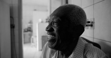 Afrika kökenli yaşlı bir adam fayanslı bir mutfakta neşeyle gülüyor, siyah beyaz bir portre, bir ev ortamında mutluluk, bağlantı ve bilgeliği vurguluyor.